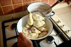 Top of a pastry chef taking out cooked dumplings from boiling water into a colander. Process of cooking dumplings step by step. Close-up, food background. photo