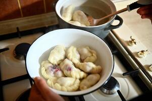 High angle view of a pastry chef taking out cooked dumplings from boiling water into a colander. Process of cooking dumplings step by step. Close-up, food background. photo