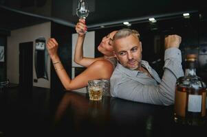 Attractive tanned European woman and handsome Caucasian middle aged man drinking alcohol and having fun together while celebrating an event at home bar. Flirt, seduction, Couple relationships concept photo