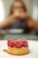 detalles en un francés postre - un tartaleta con frambuesas en un blanco lámina, terminado borroso antecedentes de un pequeño niño foto