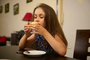 encantador niño disfrutando un delicioso francés postre, merienda con un limón tarta, sentado a mesa en el vivo habitación foto