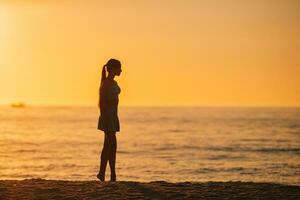 silueta de la hermosa chica disfrutando de la hermosa puesta de sol en la playa foto