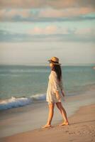 mujer hermosa joven en sombrero de paja en la playa al atardecer foto