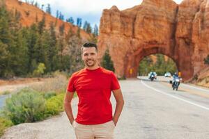 Young caucasian man in background of natural stone arch Bridge in the Red Canyon National Park in Utah, USA photo