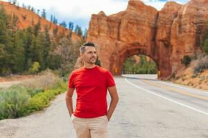 joven caucásico hombre en antecedentes de natural Roca arco puente en el rojo cañón nacional parque en Utah, EE.UU. natural Roca arco en rojo cañón, marmita nacional bosque, Utah, unido estados foto