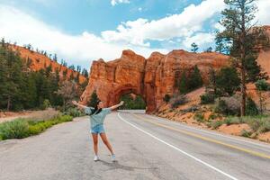 Young happy woman in background of natural stone arch Bridge in the Red Canyon National Park in Utah, USA photo