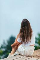 espalda ver de joven mujer sentar en un terraza a un altura en el montañas en contra el fondo de niebla y montañas foto