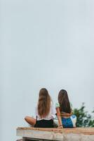 Back view of young girls sit on a terrace at a height in the mountains against the backdrop of fog and mountains photo