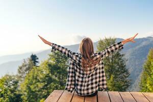 Back view of young girl sit on a terrace at a height in the mountains against the backdrop of fog and mountains photo