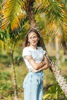a girl in a white shirt and blue jeans standing next to a palm tree photo