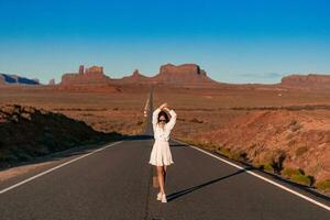 Happy young woman in white dress on the famous road to Monument Valley in Utah. Amazing view of the Monument valley. photo