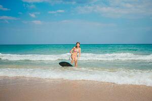 Adorable teen girl on the beach having fun in shallow water playing with board photo