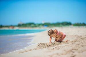 Little girl at tropical white beach making sand castle photo
