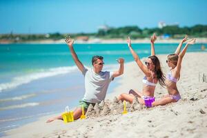 Parents and little daughter enjoying time on the beach. Family making sand castle together on the seashore photo