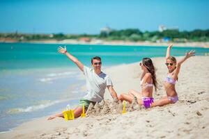 Parents and little daughter enjoying time on the beach. Family making sand castle together on the seashore photo