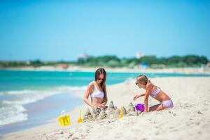 madre y hija disfrutando hora en el playa. familia haciendo arena castillo juntos en el costa foto