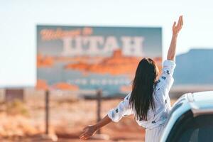 hermosa mujer en su viaje por el coche en el antecedentes de Bienvenido a Utah estado frontera firmar Derecha en el Monumento Valle foto