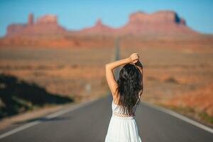 Happy young woman in white dress on the famous road to Monument Valley in Utah. Amazing view of the Monument valley. photo