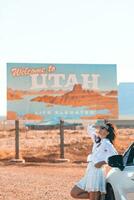 hermosa mujer en su viaje por el coche en el antecedentes de Bienvenido a Utah estado frontera firmar Derecha en el Monumento Valle foto