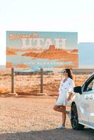 Beautiful woman on her trip by the car. Welcome to Utah road sign. Large welcome sign greets travels in Monument Valley, Utah photo