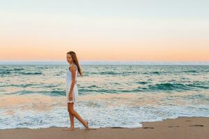 adorable adolescente niña en blanco en el costa durante su playa verano vacaciones con increíble cielo en antecedentes foto