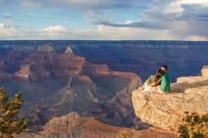 contento Pareja en un escarpado acantilado tomando en el increíble ver terminado famoso grandioso cañón en un hermosa atardecer, grandioso cañón nacional parque, Arizona, Estados Unidos foto