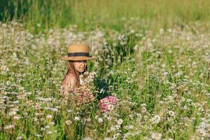 Portrait of girl in dress and straw hat on a chamomile field in summer photo