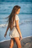 adorable joven niña con hermosa largo pelo disfrutar tropical playa vacaciones. el niña en el costa a puesta de sol foto