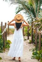 Happy woman on her way on the beach. woman in white beach dress and straw hat on summer tropical vacation photo