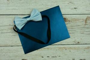 Blue bow tie with dark blue invitation card on wooden table. photo