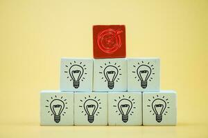 Arranging wooden blocks with red dartboard icon on top of icon many bright light bulb icon. photo