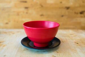 Empty red bowl on a black saucer on wood background photo
