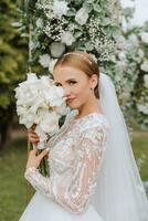 Amazing wedding bride near wedding arch. Beautiful bride in a white long dress with a veil tenderly hug near a wooden arch decorated with flowers, nature in the forest at night. photo