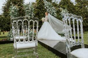 Amazing wedding bride near wedding arch. Beautiful bride in a white long dress with a veil tenderly hug near a wooden arch decorated with flowers, nature in the forest at night. photo