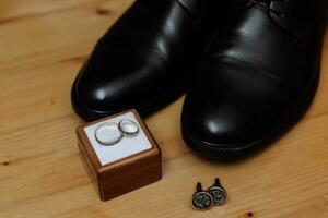 Groom's wedding day accessories. Brown leather shoes, belt, perfume, golden rings on grey background. Male fashion photo