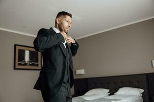 elegante novio retrato consiguiendo Listo en el Mañana para Boda ceremonia. Mañana de el novio. novio Mañana preparación. el novio pone un negro chaqueta en movimiento foto