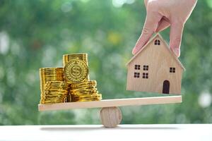 Model house with stack of gold coins money on wood scale seesaw with natural green background,Business investment and real estate concept photo