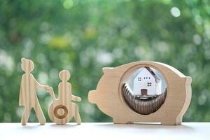 Employee volunteer assistant with man on wheelchair and model house in piggy bank on natural green background,Save money for prepare in future and handicapped person concept photo