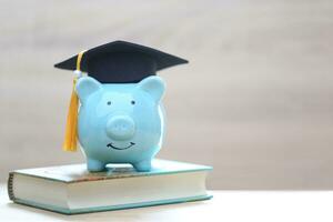 graduación sombrero en cerdito banco y un libros en blanco fondo, ahorro dinero para educación concepto foto