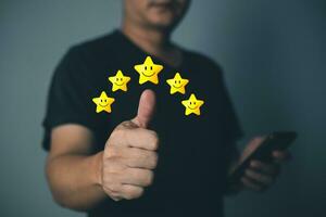 a man thumbs up on the happy smile face icon and five star to give satisfaction in service.rating very impressed.Customer service and Satisfaction concept. photo