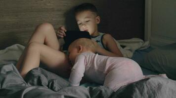 A boy with a tablet and his baby sister on a messy bed video