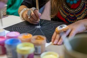 Woman's hands with jewelry draw a colorful mandala on black paper. photo