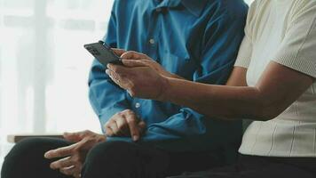 gelukkig senior oud paar Holding smartphone op zoek Bij mobiele telefoon scherm lachend ontspannende zitten Aan sofa samen, glimlachen ouderling volwassen grootouders familie omarmen hebben pret met mobiel telefoon Bij huis video