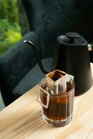 Glass cup with making coffee from drip bag on wooden table. Trends in making coffee at home. photo