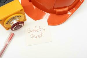 Orange safety hat with message Safety First, Red Pen and Emergency Stop Button isolated on white background. Safety First Concept. Copy Space for text. photo