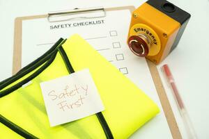 Safety First message on paper. Reflective vest, safety hat or helmet and Emergency Stop Button. Safety First Concept. Blank checklist paper during safety audit and risk verification. photo