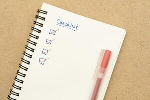 Top view of notebook with handwritten Checklist text and red pen. Checklist concept, checklist box with red checkmark. Blank checklist for text. photo