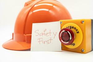 Orange safety hat with message Safety First and Emergency Stop Button isolated on white background. Safety First Concept. photo