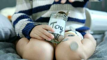 Asian boy sits and puts coins in a glass jar to save money to buy toys. video