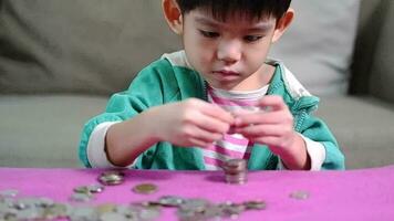 asiatisch Junge arrangieren Münzen im ein Reihe zu trainieren Speichern Geld video